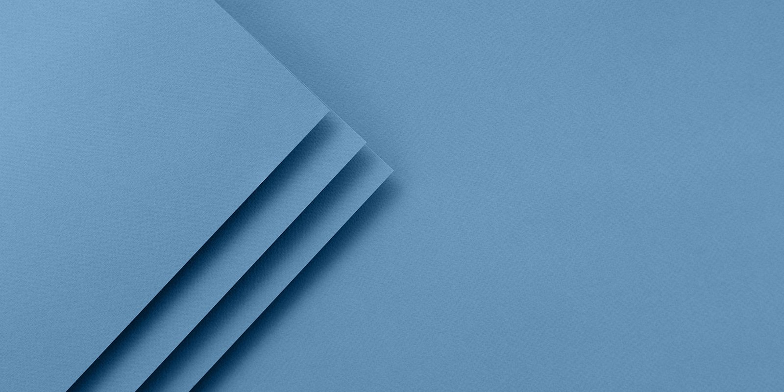 Feuilles de papier bleu superposées en angle, sur fond du même bleu.