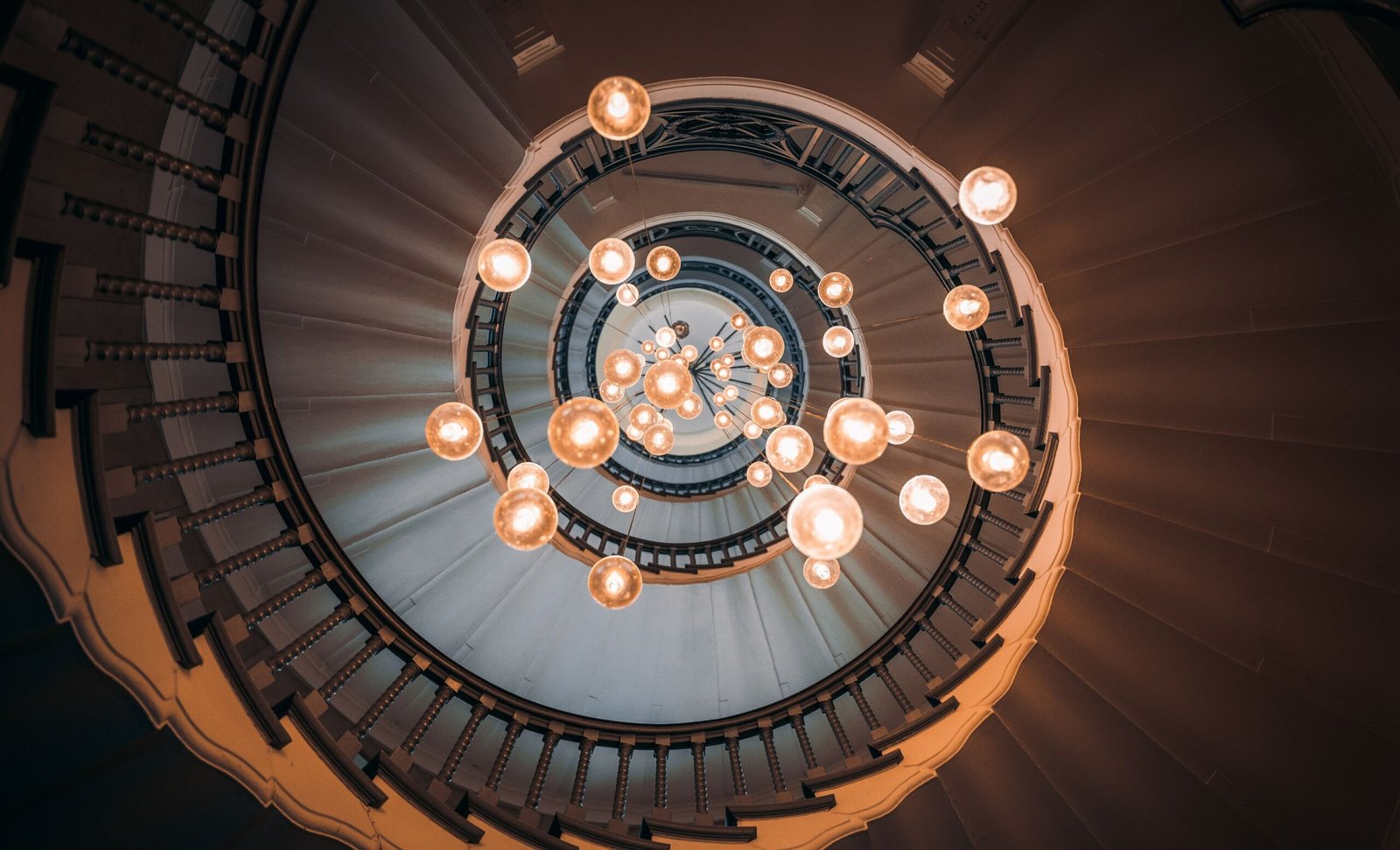 Hebras Avocats. Escalier hélicoïdal du cabinet Hebras vu du dessous, éclairé par une nuée de globes lumineux suspendus.